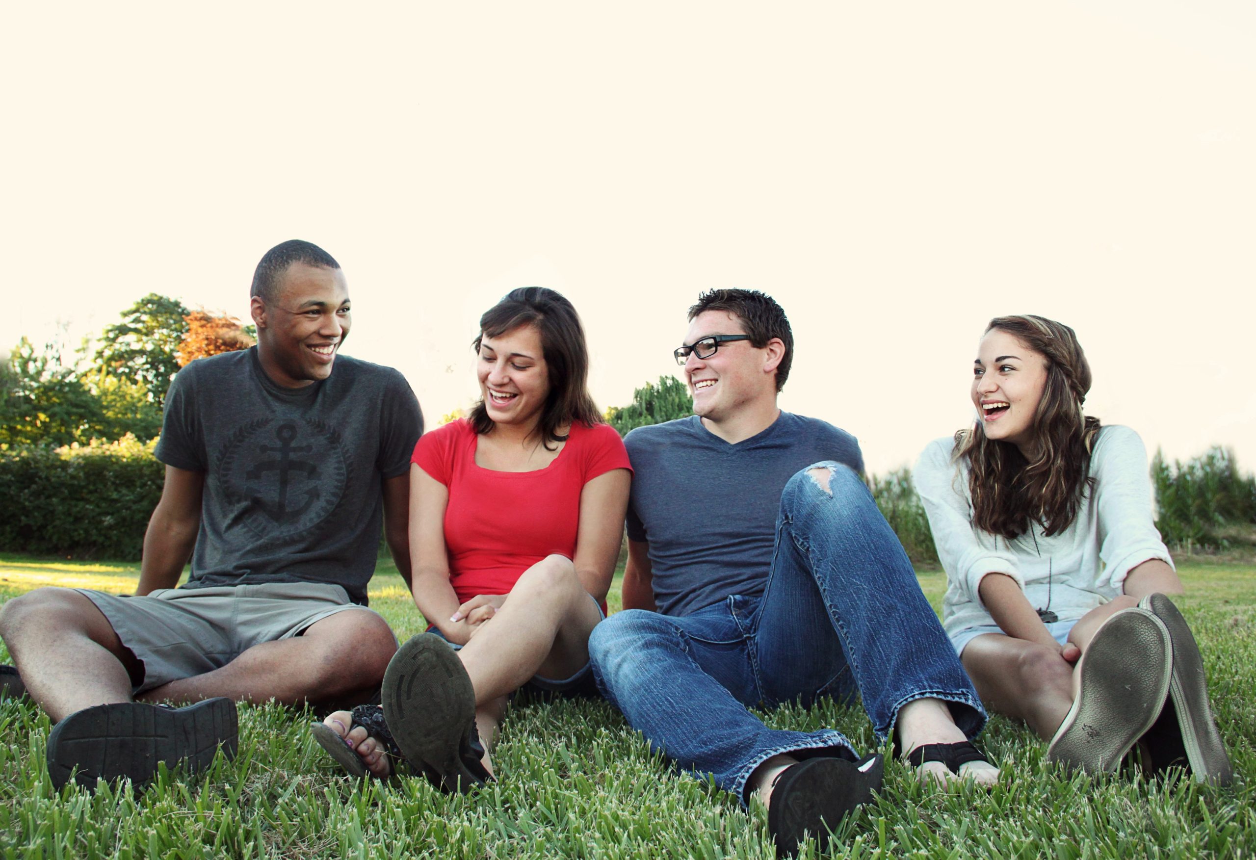 smiling-women-and-men-sitting-on-green-grass-1231230
